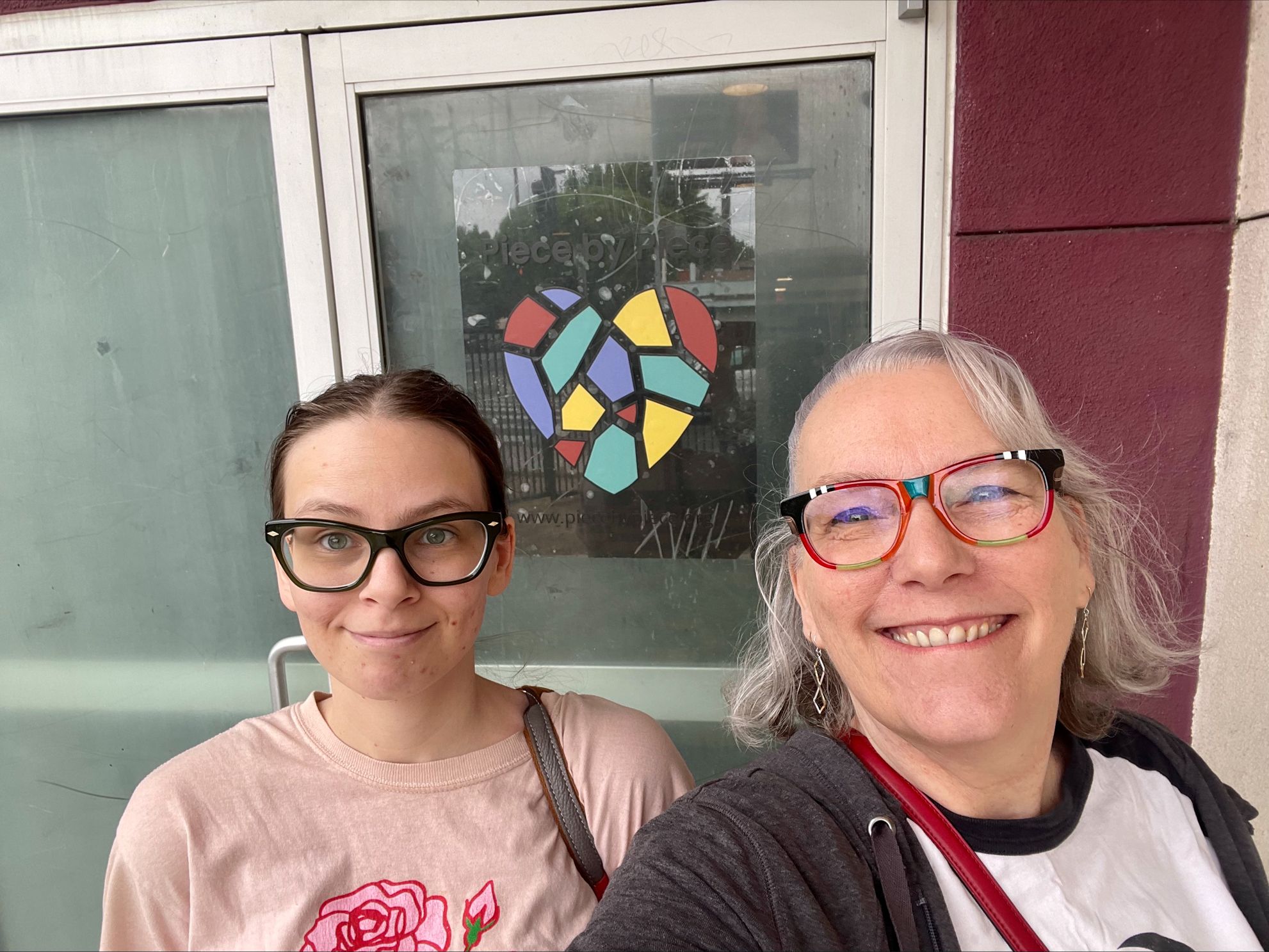 Two volunteers take a selfie in front of the Piece by Piece door.