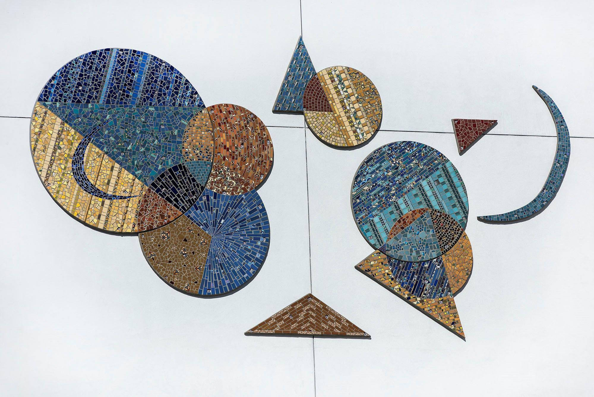 A large mosaic made up of geometric shapes intersecting. Circles, triangles, and half moons in blues and yellows.