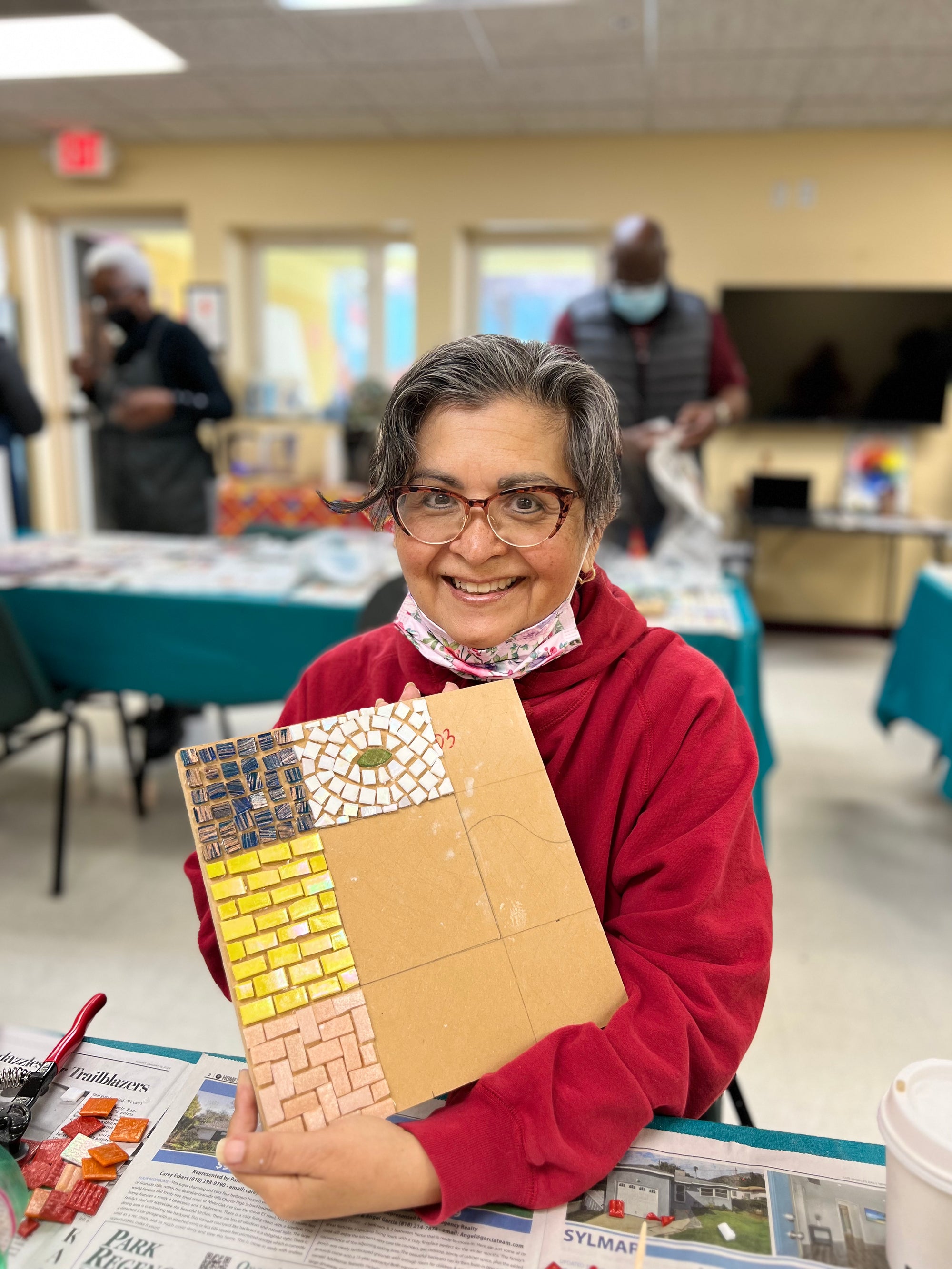 Artist smiling and holding up a half-finished mosaic of squares.