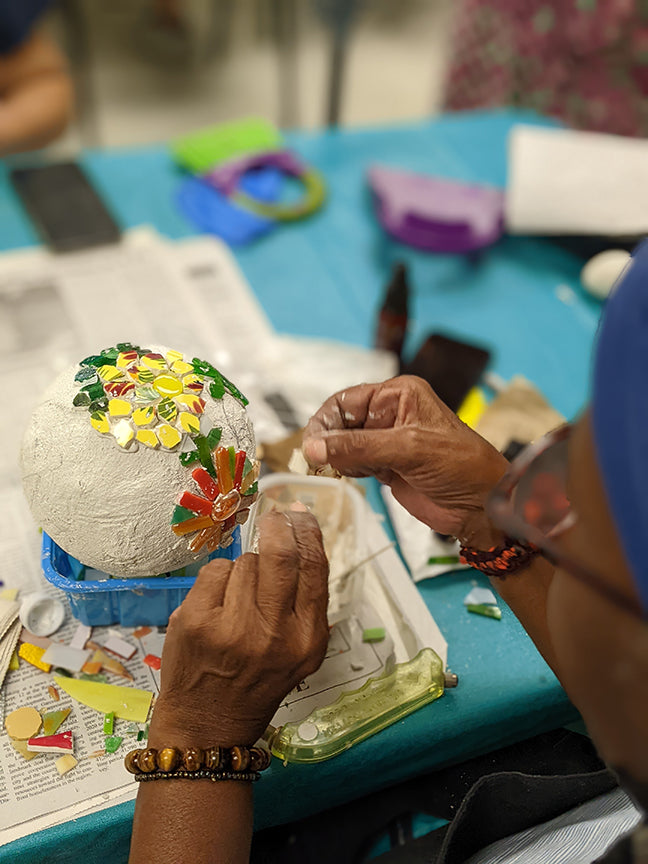 Artist working on placing mosaic flowers on a sphere at a mosaic workshop.