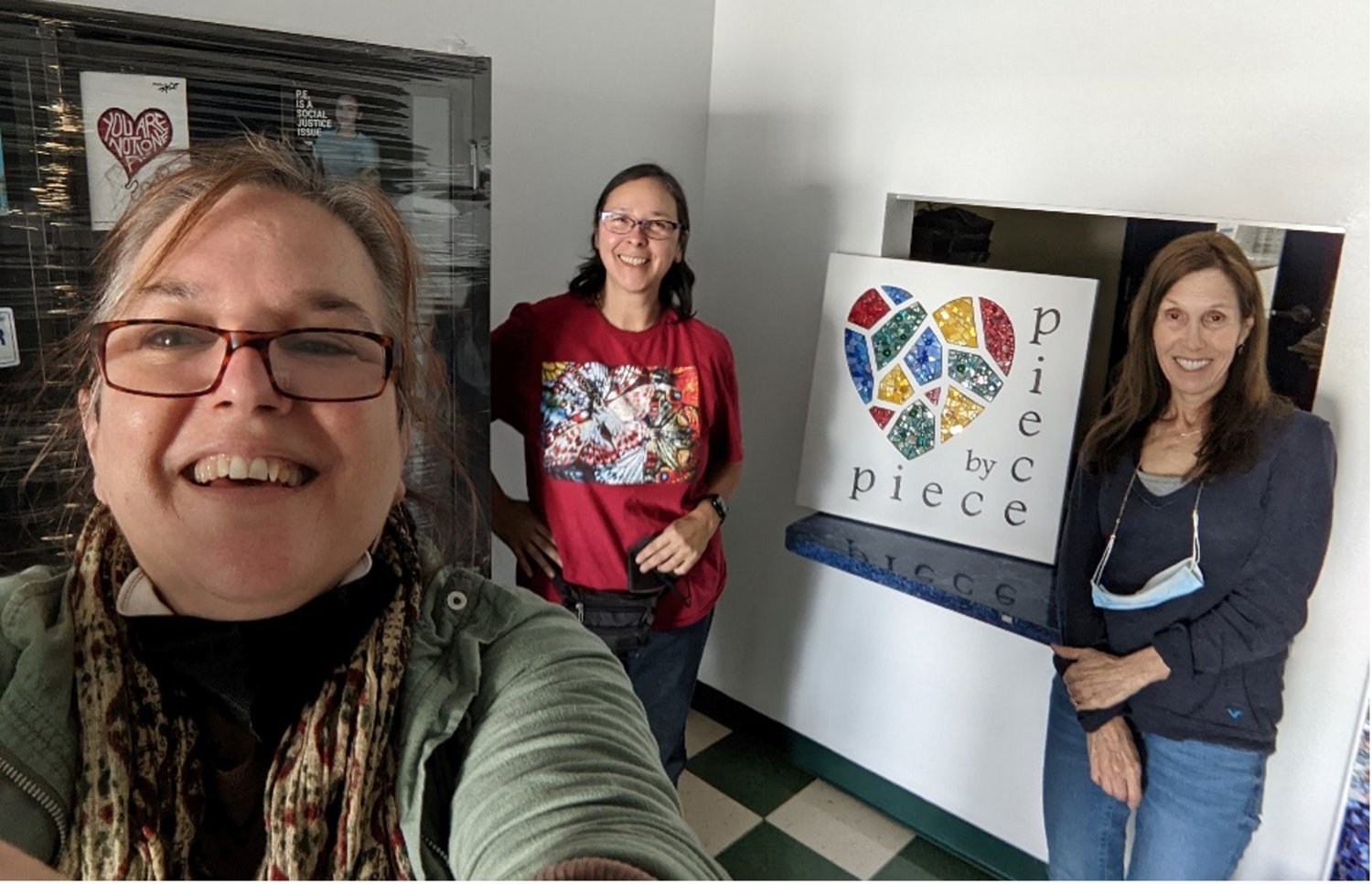 Three members of the Piece by Piece staff take a selfie with a mosaic of the Piece by Piece logo.