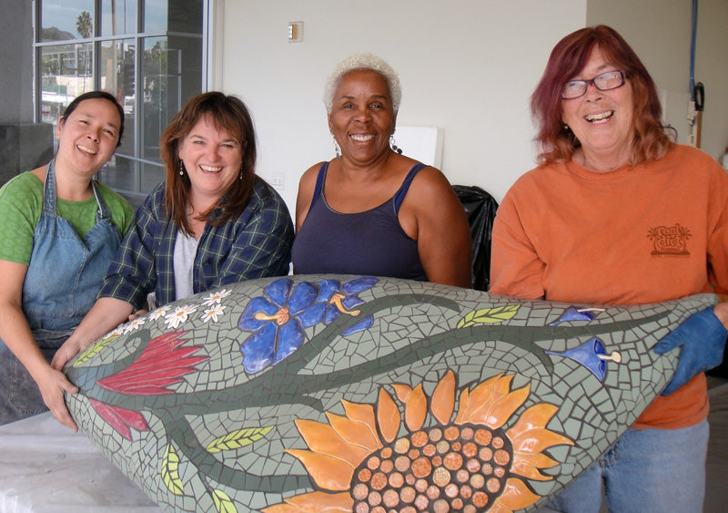 A group of artist instructors holding a large 3D mosaic leaf.