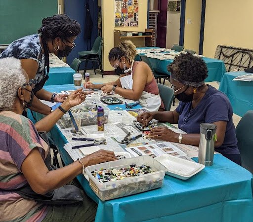 A group of artists working on mosaic projects at a table in the Piece by Piece studios.