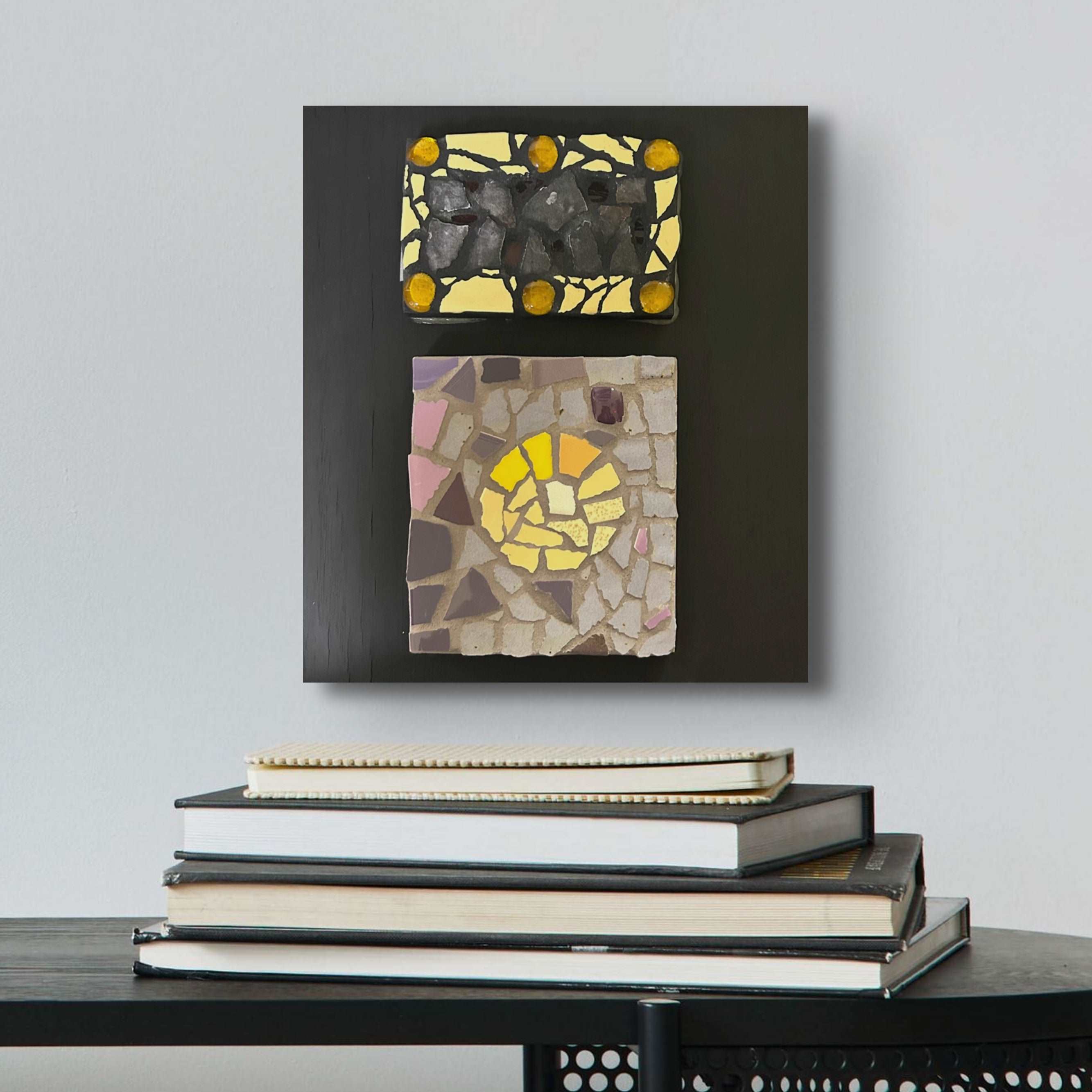 Two panel mosaics of yellow and black tiles, one above the other, on a plank of wood painted black. 