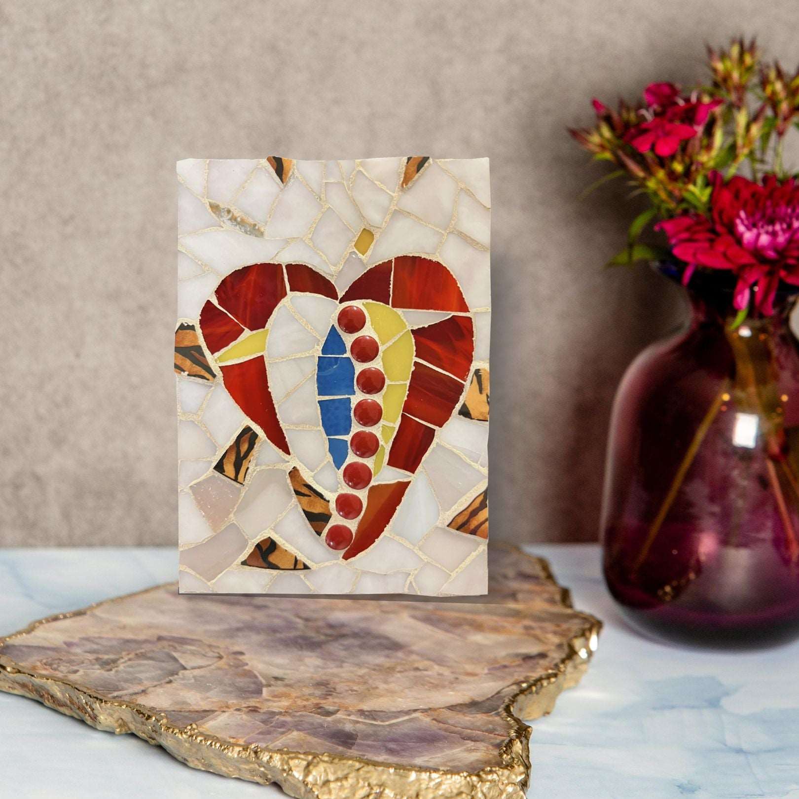 Abstract mosaic heart made up of red, blue, and yellow pieces with a muted pearly background and golden accents. 
