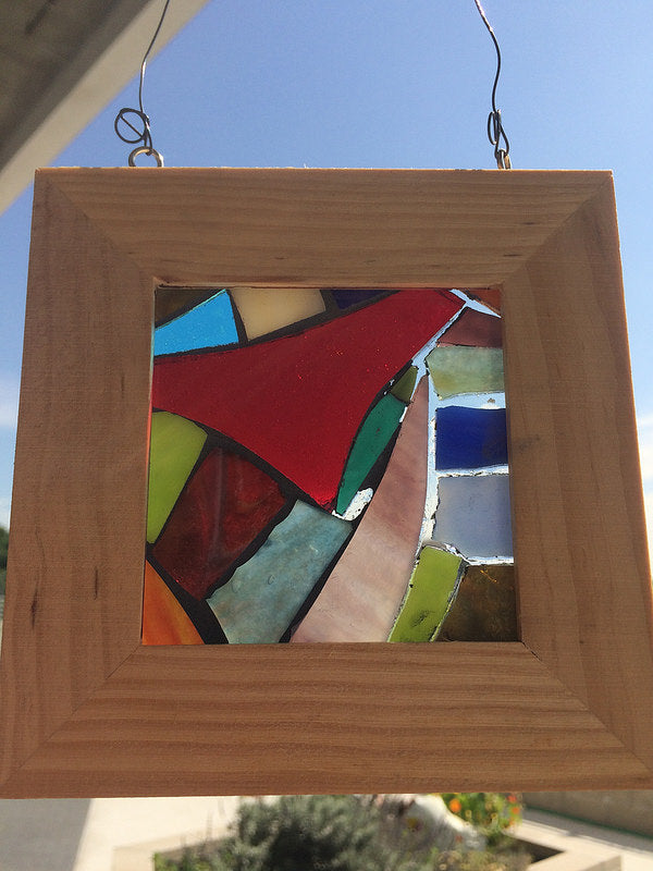 Colorful mosaic in a wood frame with light shining through. 